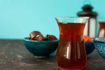 Turkish sweets dried dried apricots, prunes, marshmallows, nuts lie in a blue bowl, and Turkish tea is nearby. Black textural background and blue wall. Oriental hospitality.