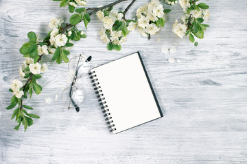 Empty sheet of notepad with glasses on a white wood background with blossom flowers. Copy space for spring text.