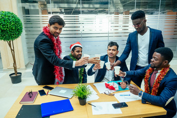 happy group of indian and african american people drinking toast from cup,wearing santa hat and...