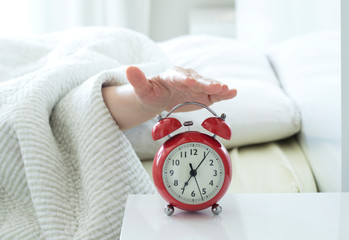 young woman sleeping on bed pressing snooze button on black vintage alarm clock at seven o'clock...