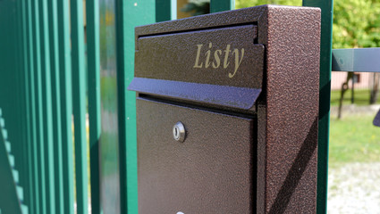 Skrzynka pocztowa zainstalowana na płocie budynku mieszkalnego. Napis na skrzynce oznacza w tłumaczeniu oznacza "listy". 
