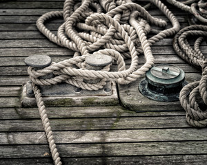 Obraz premium Three bollards on a wood deck with mooring lines rolled up around it