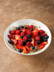Oatmeal flakes breakfast with fresh berries - strawberry and blueberry  on homemade background and natural morning light.