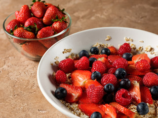 Oatmeal flakes breakfast with fresh berries - strawberry and blueberry  on homemade background and natural morning light.