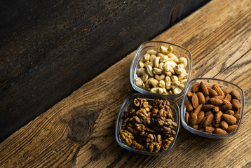 Almond, walnut and cashew in a small plates which standing on a wooden vintage table. Nuts is a healthy vegetarian protein and nutritious food. Nuts on rustic old wood.