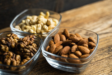 Almond, walnut and cashew in a small plates which standing on a wooden vintage table. Nuts is a healthy vegetarian protein and nutritious food. Nuts on rustic old wood.