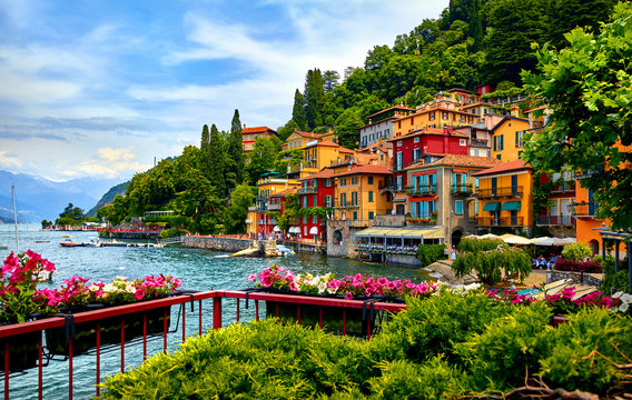 Varenna, Italy. Picturesque town at lake Como. Colourful motley Mediterranean houses at stone beach coastline among green trees. Popular health resort and touristic location. Summer day landscape.