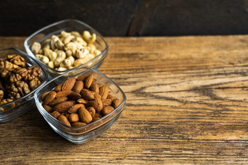 Almond, walnut and cashew in a small plates which standing on a wooden vintage table. Nuts is a...