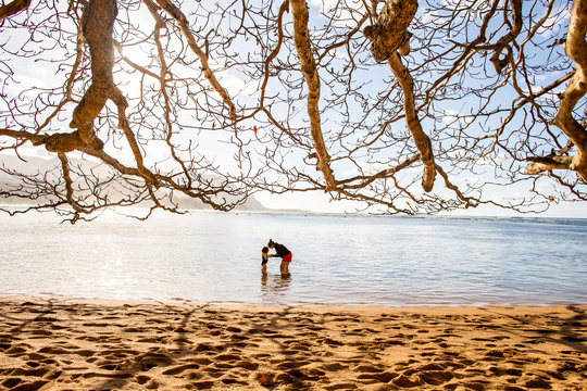 A mother and daughter playing together in the ocean on the island of Kauai in Hawaii on a sunny day.