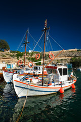 Fishing boats moored in crystal clear turquoise sea water in harbour in Greek fishing village of Mandrakia, Milos island, Greece