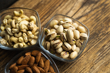 Almond, pistachio and cashew in a small plates which standing on a wooden vintage table. Nuts is a healthy vegetarian protein and nutritious food. Nuts on rustic old wood.