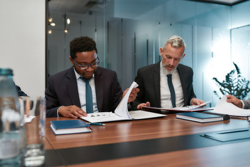 Examing documents. Caucasian and african mature businessmen reading documents while having a meeting in the office