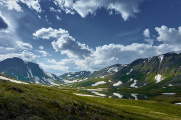 A lake surrounded by mountains with snow and green fields in summer.