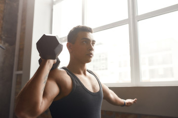 Young athletic man lifting dumbbell while having workout at industrial gym. Sport, healthy lifestyle concept