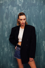 portrait of a beautiful fashionable blonde woman in a black jacket at the gray wall