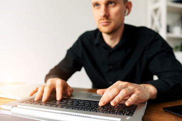 Close-up portrait of young man in smart casual shirt is using laptop for work. Male hands on keyboard. Freelancer, developer