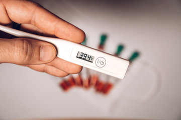 Electronic thermometer with high temperature on the screen with test tubes with blood on background