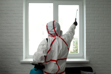 A man in a protective suit cleans the window with a chemical agent, protecting the house from...