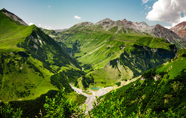 High and green mountains of Georgia. Sunny summer, blue sky. Mountain lake of blue color. Horizontal landscape.