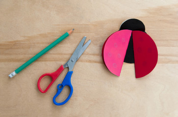 How to make cardboard colourful ladybug DIY. Homemade craft with ladybug tutorial. Glue, paper, scissors and pencil on a wooden table. Children's art project, a craft for children. Step three