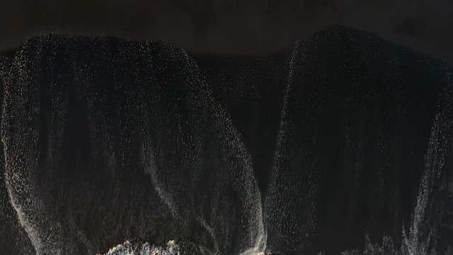 Stunning aerial footage of waves breaking against black sand beach.