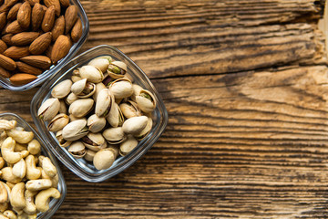 Almond, pistachio and cashew in a small plates which standing on a wooden vintage table. Nuts is a healthy vegetarian protein and nutritious food. Nuts on rustic old wood.