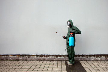 disinfection of the city from coronavirus, a man in a protective suit and a respirator against the background of the city wall, a sanitary worker