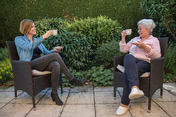 Senior woman and daughter having coffee at safety distance in the garden, 