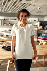 You would like it. Young woman smiling at camera, while trying on t shirt, standing in the store....