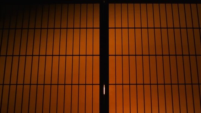 Man silhouette doing karate in kimono sleeves behind sliding paper doors with orange backlight martial arts in wooden traditional Japanese house at night in slow motion