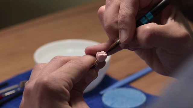 Dental technician applies ceramic material to the crown of a dental implant in a dental laboratory using tweezers and a brush. Dental technology close-up.
