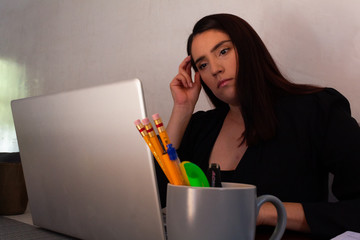 Young Hispanic woman in black clothes doing home office with a white laptop, bored and stressed...