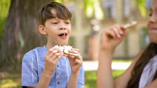 Two kids boy and girl sitting outdoors and eat their sandwiches that mothers gave them for lunch at school. Kids having fun on a lunch break eating their food. Prores 422