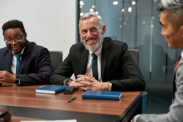 Portrait of cheerful mature businessman in formal wear looking at camera and smiling while having a meeting in the modern office
