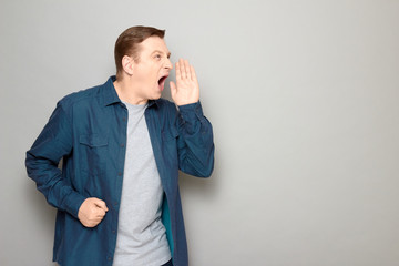 Portrait of angry mature man screaming loudly with hand near mouth