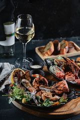 Fresh seafood and white wine on a stone table. Oysters, prawns and scallops, squids, served by the chef, beautifully laid out on plates, dark concrete background.