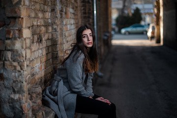 Girl in a red blouse and a gray cardigan on the background of the old brick wall