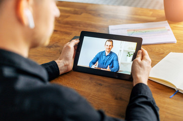 Video call on tablet screen. Male hands are holding digital tablet, a man in shirt on the screen. Online meeting, online communication