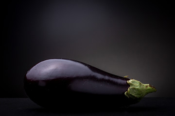 Bright reflective peel of colourful vibrant purple eggplant aubergine vegetable with green tops fresh from the local Brazilian market. Low key studio still life against a dark grey background.