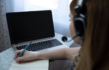 young american teen girl wear headphones video calling on laptop. pretty woman student looking at computer screen watching webinar or doing video chat by webcam