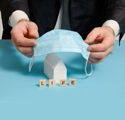 a man in a suit covers a house model with mask. family home insurance.