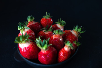 Fresh juicy strawberries in a black plate on a black matte background