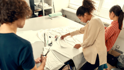 We always choose quality material. Young female fashion designer measuring fabric, textile material before cutting it in a studio. Group of creative millennials working together