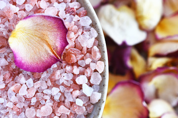 A close up image of pink Himalayan bath salt with yellow and red dried rose petals. 