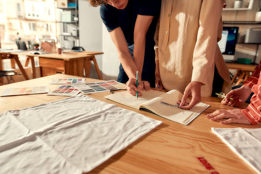 The printing professionals. Cropped shot of designers drawing sketches, while creating logo and design of T-shirt. Young man and women working together at custom T-shirt, clothing printing company