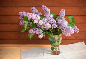 Branches of lilac in vase on rustic wooden table