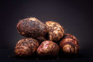 A lot of hairy brown pink raw Yam edible vegetable from the local Brazilian market against a dark grey background. Studio low key food concept still life.