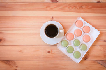 Cup of coffee and box of colorful macaroon cookies on wooden table.