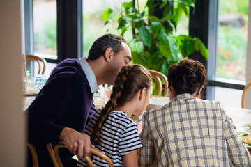 Fototapeta premium A family reading something at the kitchen table, view from the b
