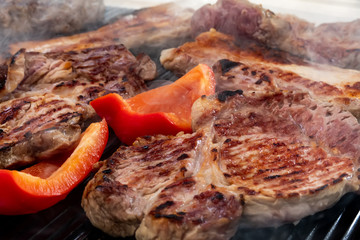Preparation of steaks on an electric barbecue grill. Appetizing pieces of beef, red pepper and pork on a electric grill.